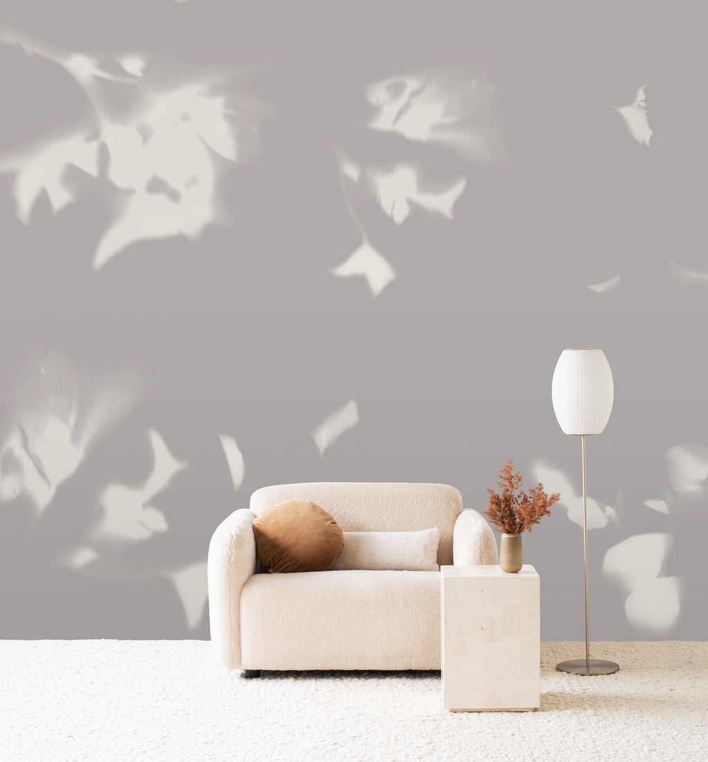 Drift wall mural by Emma Hayes in Dusk, cream foliage silhouettes on a soft mauve-grey ground behind a boucle sofa