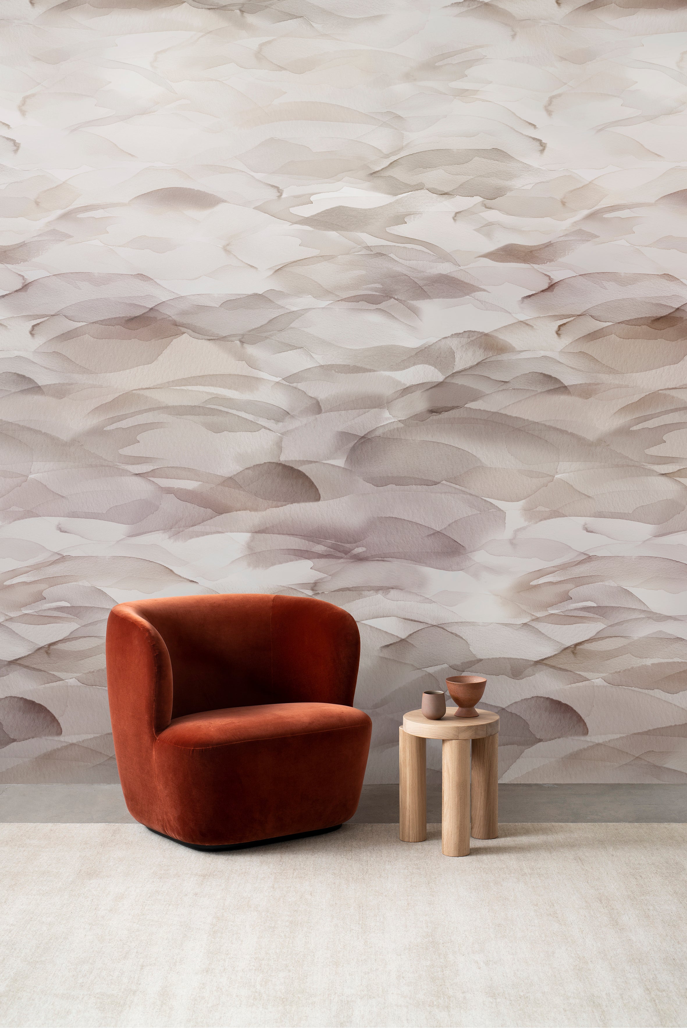 Dune wall mural by Emma Hayes in Plum, warm grey-taupe watercolour dune layers behind a rust velvet armchair