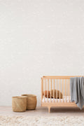 Falling Feather wallpaper by Emma Hayes, scattered white feather motif on a soft cream ground in a nursery with a wooden cot and woven baskets
