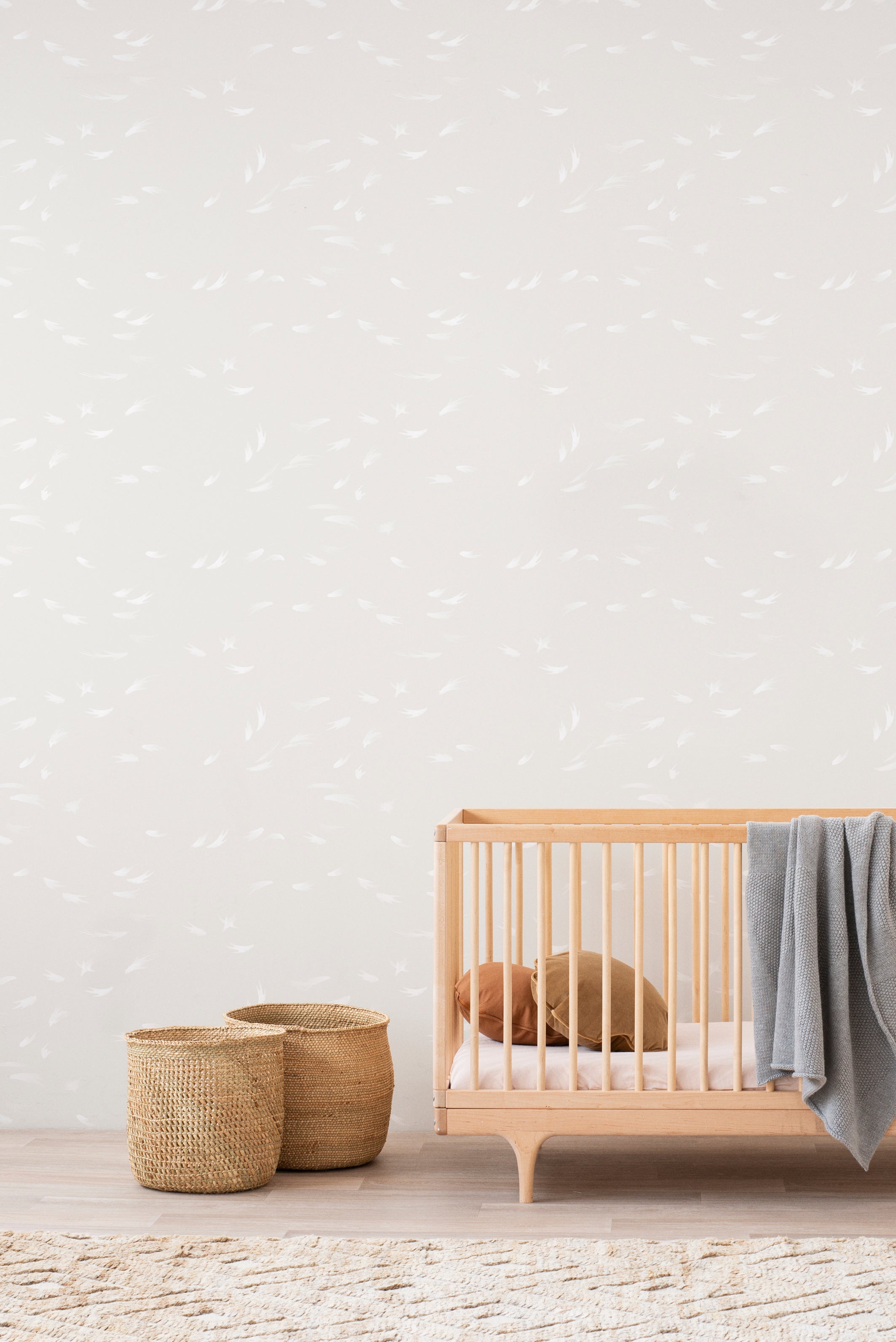 Falling Feather wallpaper by Emma Hayes, scattered white feather motif on a soft cream ground in a nursery with a wooden cot and woven baskets