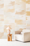 Mirage wallpaper by Emma Hayes in warm gold, an abstract brushstroke design, styled beside a cream boucle sofa and table lamp