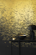 Reflection wallpaper by Emma Hayes in metallic gold on black, shimmering light-on-water ripples, styled behind a dark console with a brass bowl and lamp