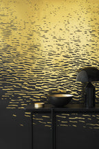 Reflection wallpaper by Emma Hayes in metallic gold on black, shimmering light-on-water ripples, styled behind a dark console with a brass bowl and lamp