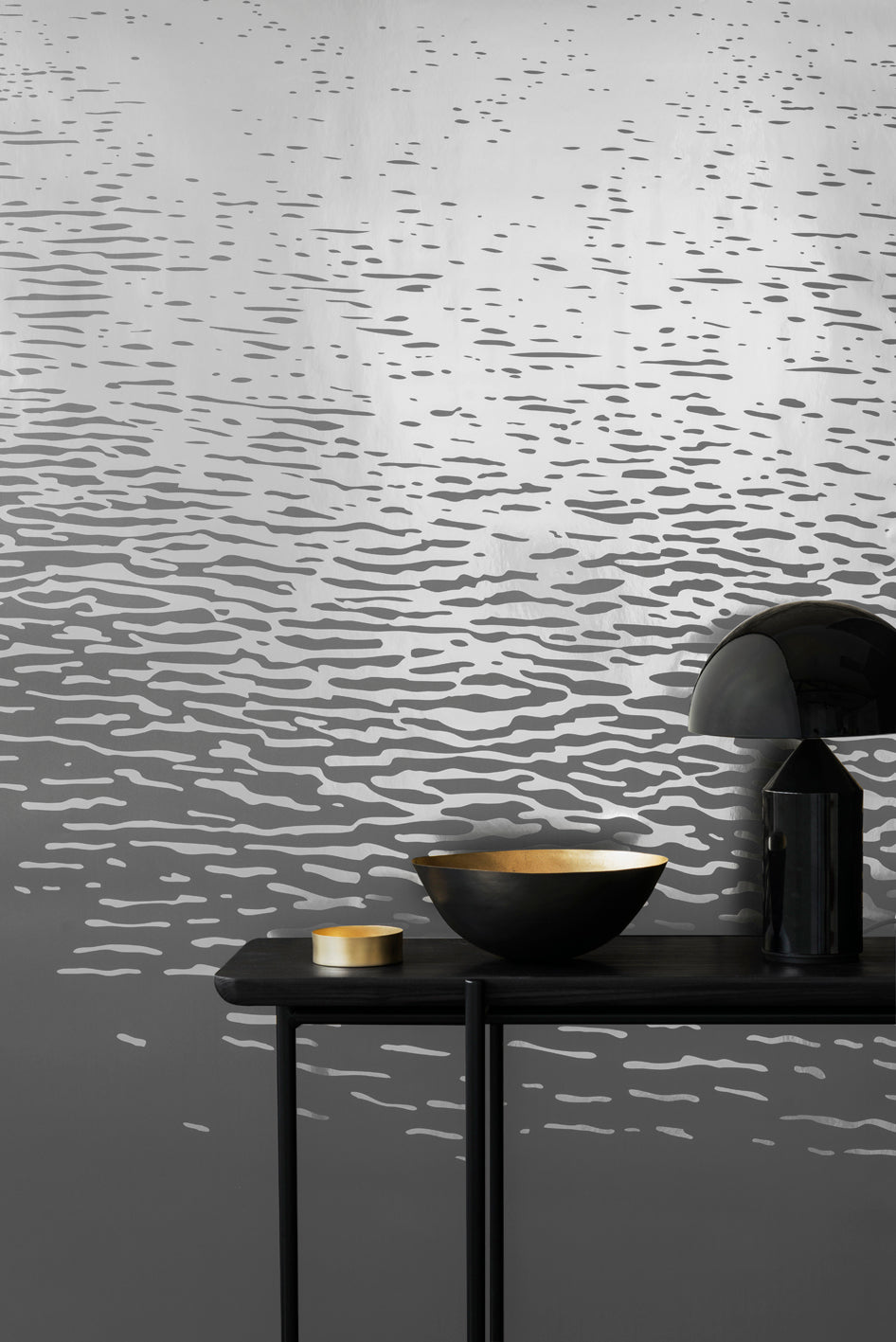 Reflection wallpaper by Emma Hayes in metallic silver on grey, rippling water-reflection pattern, styled behind a black console with a bowl and lamp