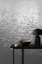 Reflection wallpaper by Emma Hayes in metallic silver on grey, rippling water-reflection pattern, styled behind a black console with a bowl and lamp