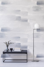 River wall mural by Emma Hayes, pale watercolour washes in blue-grey across a feature wall behind a dark bench with eucalyptus and books