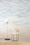 Sandscape wall mural by Emma Hayes in Sand, soft watercolour brushstrokes graduating from sky blue to warm beige, styled behind a white floor lamp and side table