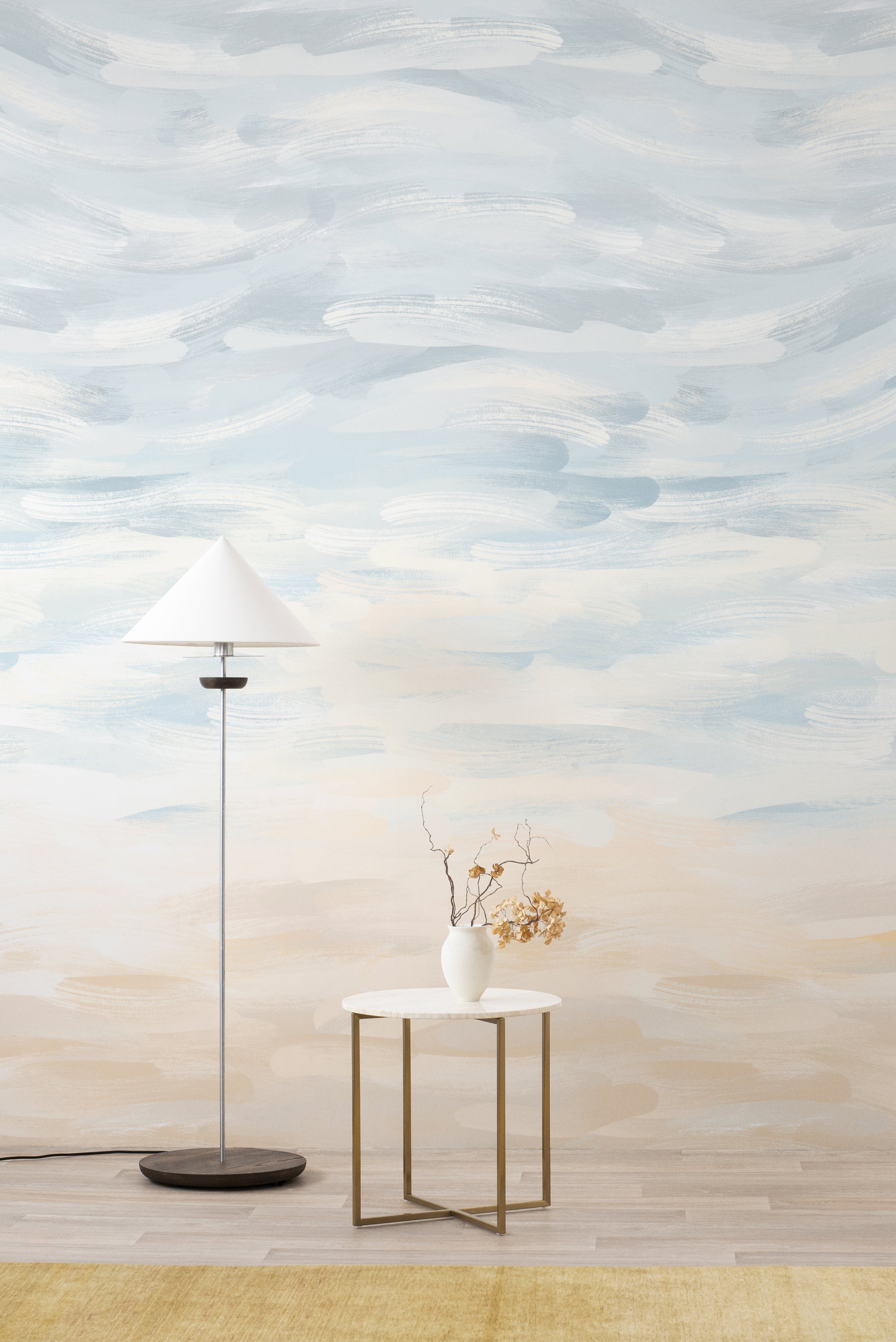 Sandscape wall mural by Emma Hayes in Sand, soft watercolour brushstrokes graduating from sky blue to warm beige, styled behind a white floor lamp and side table