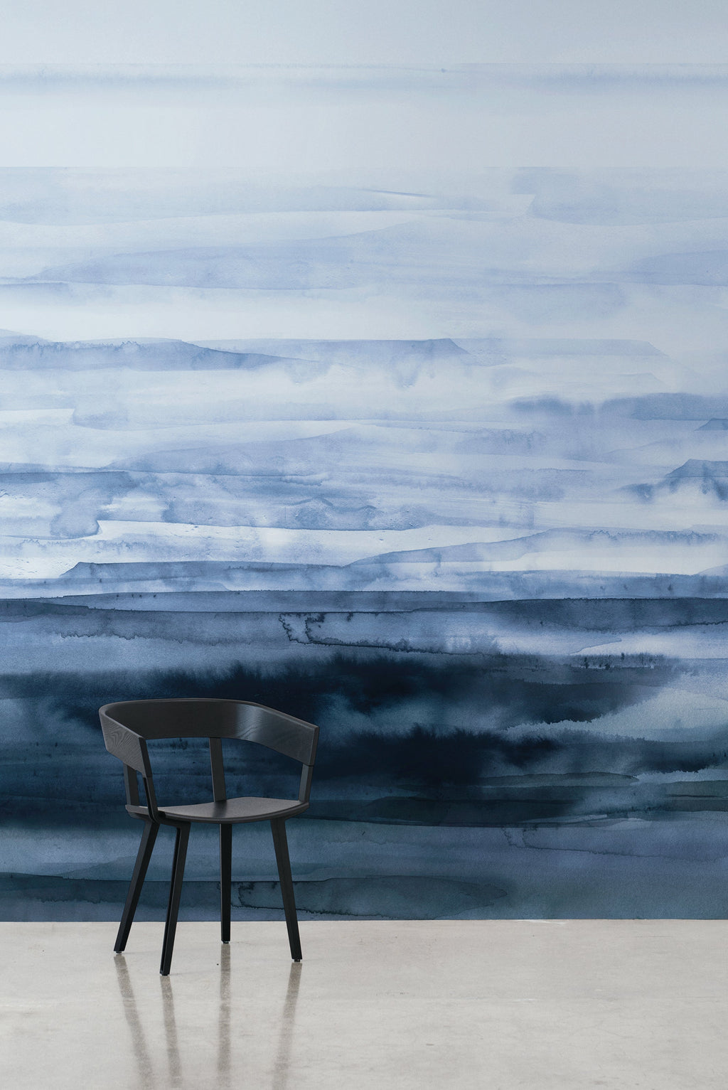 Sediment wall mural by Emma Hayes in Blue, horizontal watercolour strata fading from pale sky to deep indigo, styled with a black chair against a polished floor