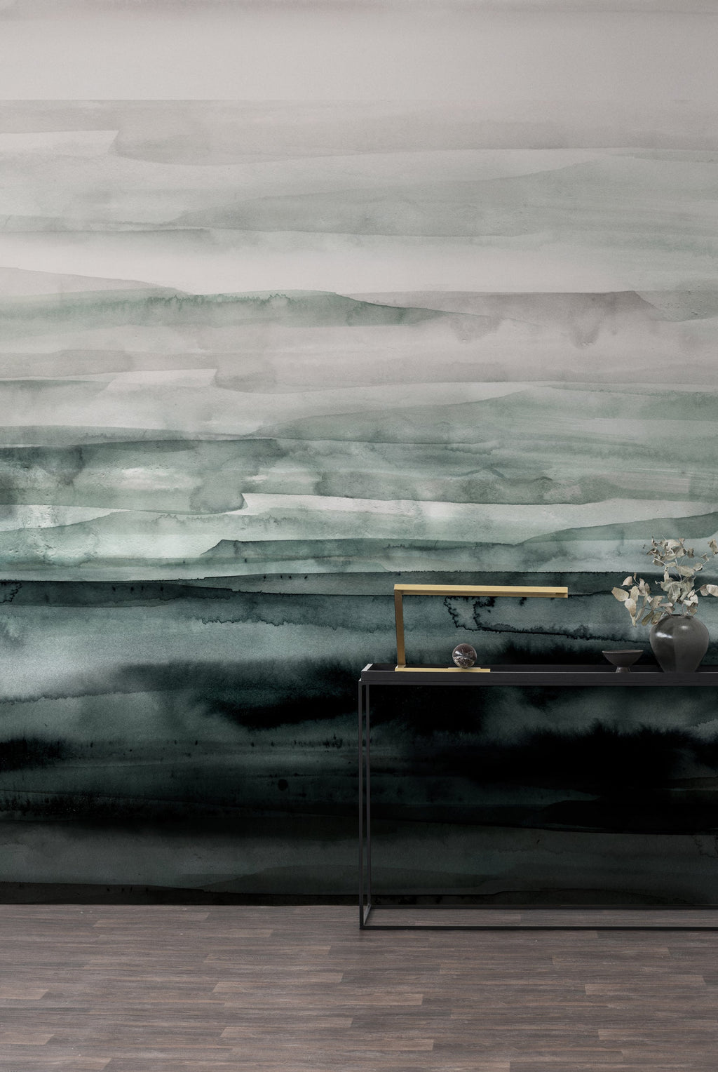 Sediment wall mural by Emma Hayes in Forest, misty grey-green watercolour strata deepening to near-black, styled behind a black console with brass lamp