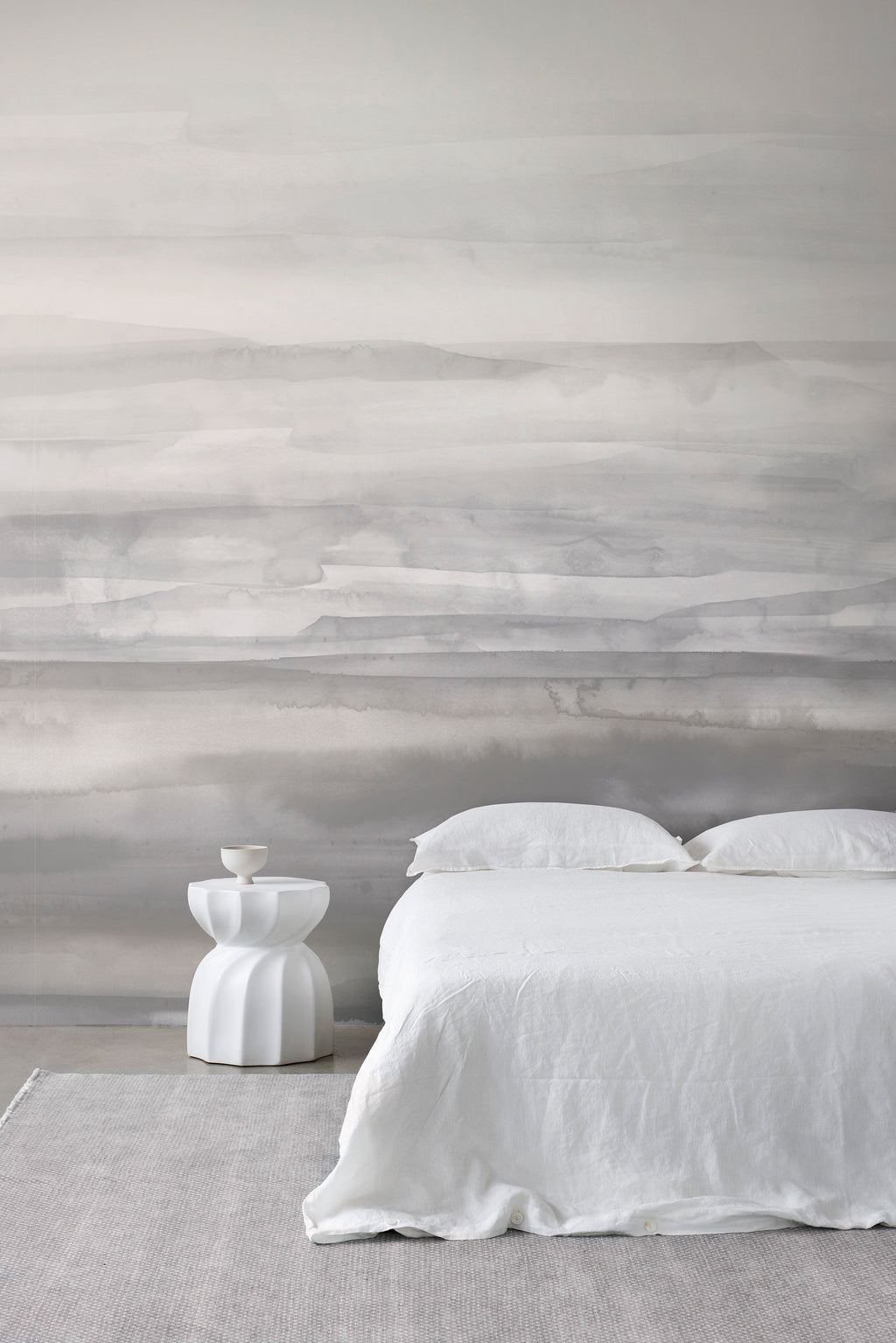 Sediment wall mural by Emma Hayes in Greystone, soft tonal grey watercolour bands styled in a serene bedroom with white linen and pale rug