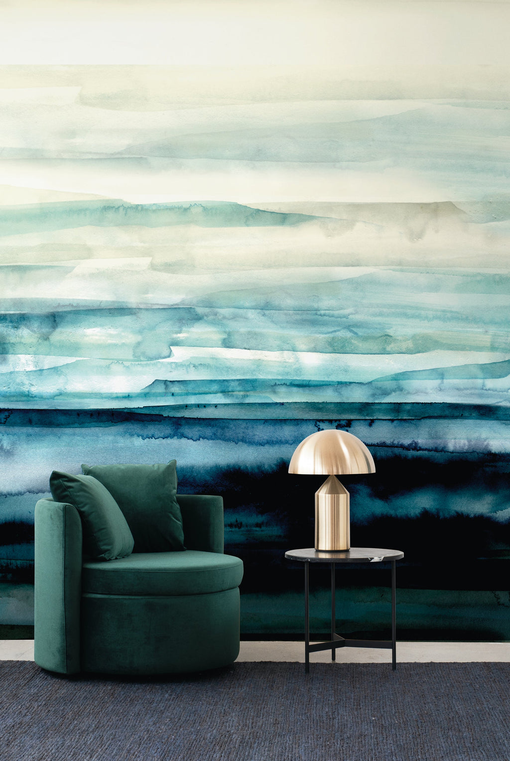 Sediment wall mural by Emma Hayes in Turquoise, aqua and teal watercolour layers over deep blue, styled with a green velvet armchair and brass lamp