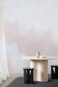 Solar wall mural by Emma Hayes in Heaven, dreamy blush-pink and lilac haze behind a sculptural stone dining table and black stools