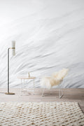 Tussock wall mural by Emma Hayes, sweeping grass strands in cool grey and white, styled with a sheepskin wire chair and side table