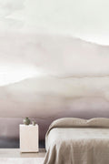 Wash wall mural by Emma Hayes in dusty plum and mauve watercolour wash, styled behind a neutral linen bed with stone side