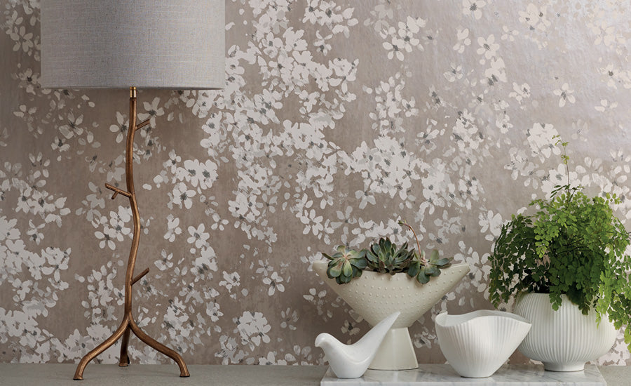Tiami wallpaper by Romo, white blossom on a taupe ground, styled behind a brass tree lamp with potted ferns