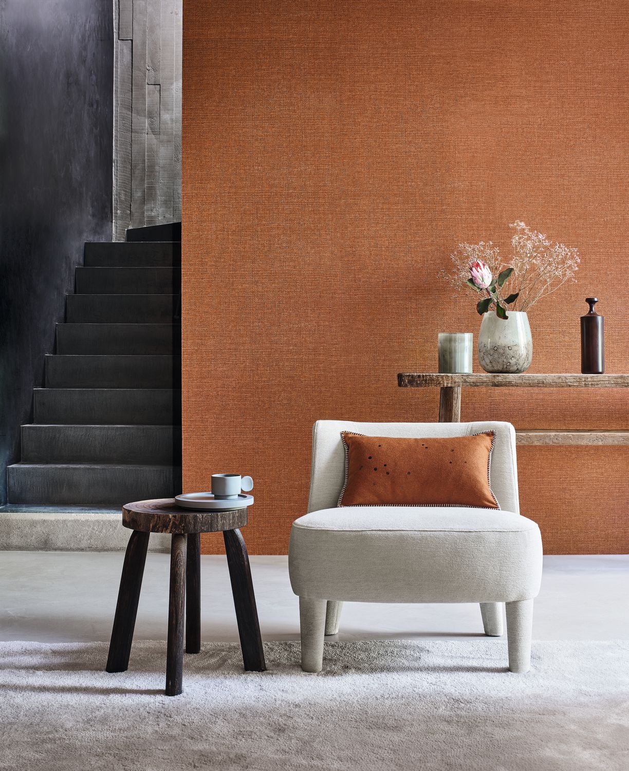 Carioca wallpaper by Casamance in burnt orange, a plain woven texture styled beside a black stone staircase with a cream boucle chair