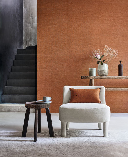Carioca wallpaper by Casamance in burnt orange, a plain woven texture styled beside a black stone staircase with a cream boucle chair