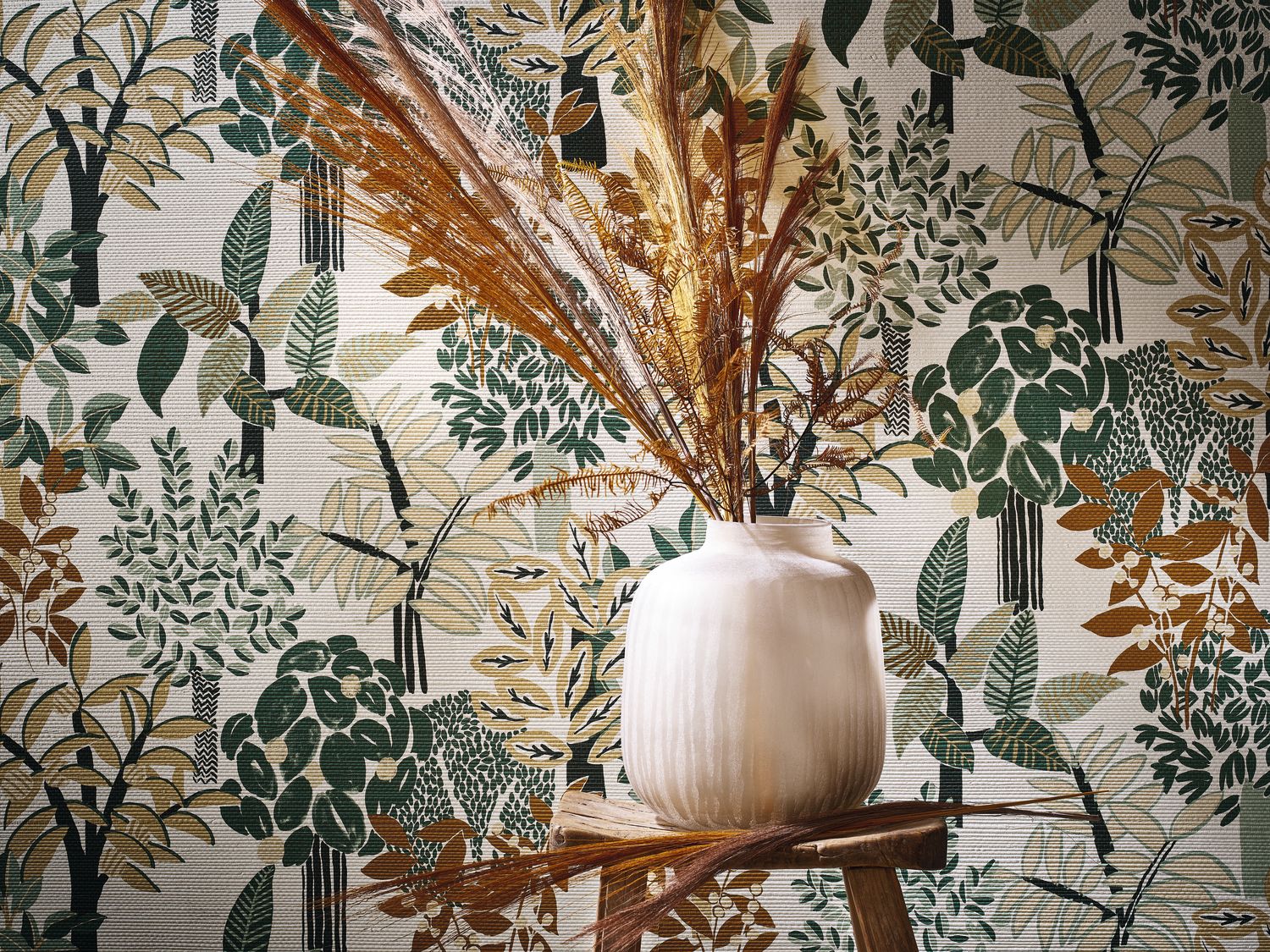 Peradeniya wallpaper by Casamance in white and emerald, a woodland foliage print styled behind a ribbed ceramic vase of dried palm fronds