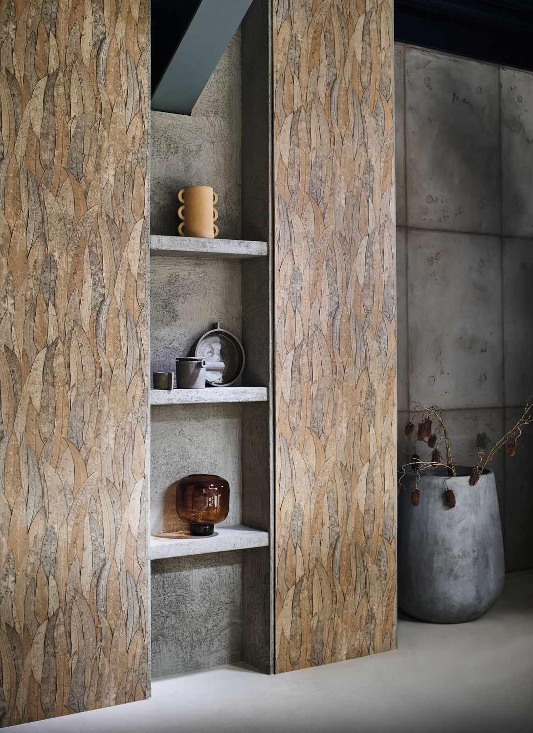 Neluwa wallpaper by Casamance in bronze, an overlapping leaf texture styled on tall panels beside concrete shelving