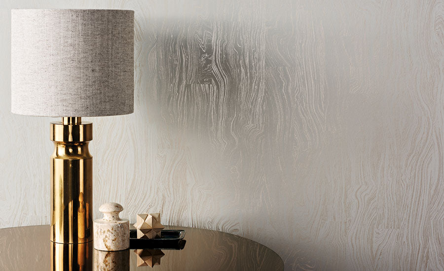 Otishi wallpaper by Romo, a pale marbled wood-grain sheen, styled beside a gold column lamp
