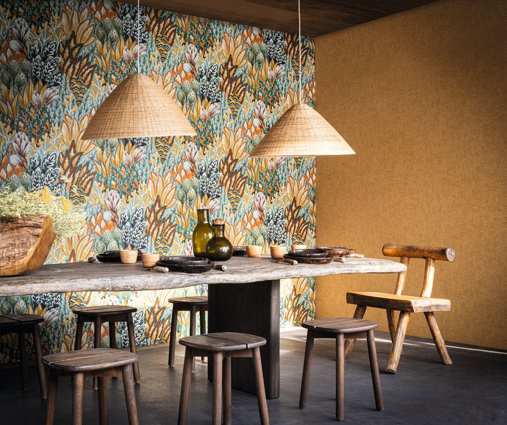 Avicennia wallpaper by Casamance in emerald and mustard, a dense protea and foliage print styled in a dining room with woven rattan pendants and a stone table