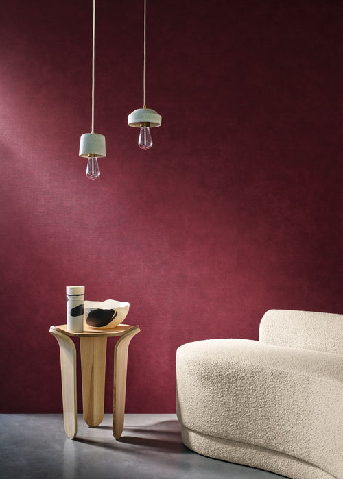 Argile wallpaper by Casamance in deep burgundy, a plain chalky texture styled behind a cream boucle sofa with glass pendant lights
