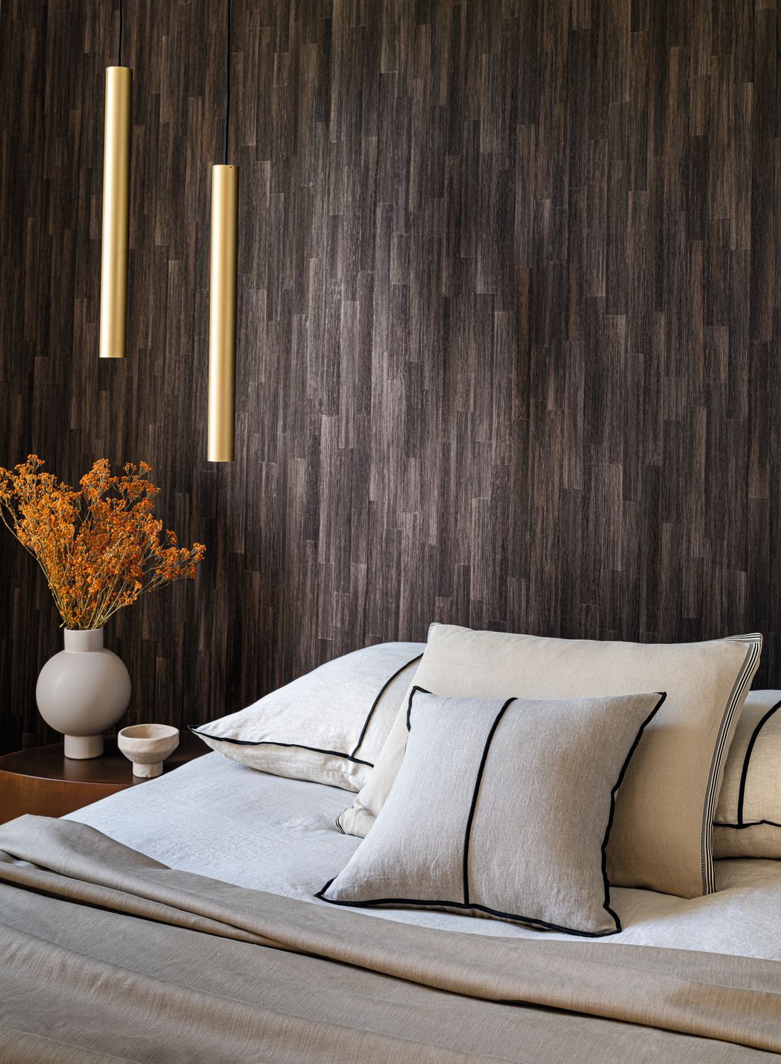 Sapelli wallpaper by Casamance in ebony, a timber plank effect styled behind a bed with white linen and slim brass pendant lights