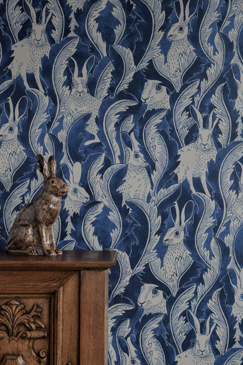 Hiding Hares wallpaper by Emma von Brömssen in Dark Denim, blue and cream hares among leaves with a hare figurine on a