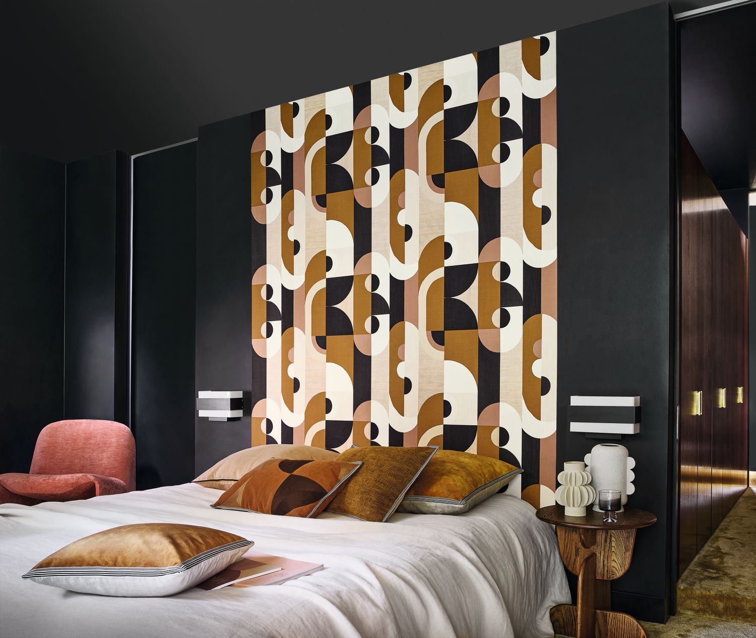 Vassily wallpaper by Casamance in bronze and ochre, a bold geometric design styled on a panel behind a bed in a dark room