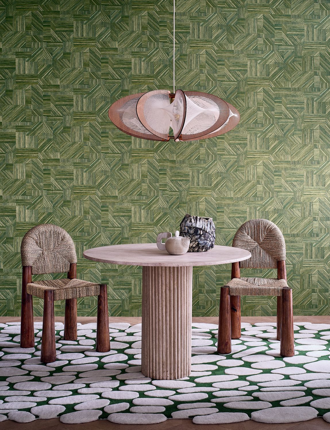 Imbrication wallpaper by Casamance in moss green, a woven parquet geometric styled behind a round fluted table and woven chairs