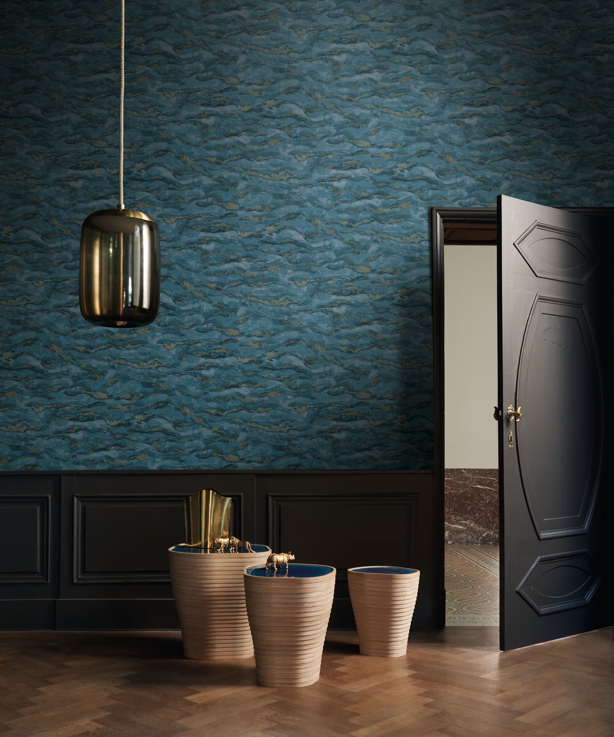 Sohar wallpaper by Casamance in navy and gold, a rippling wave texture styled beside a panelled door with ceramic vessels