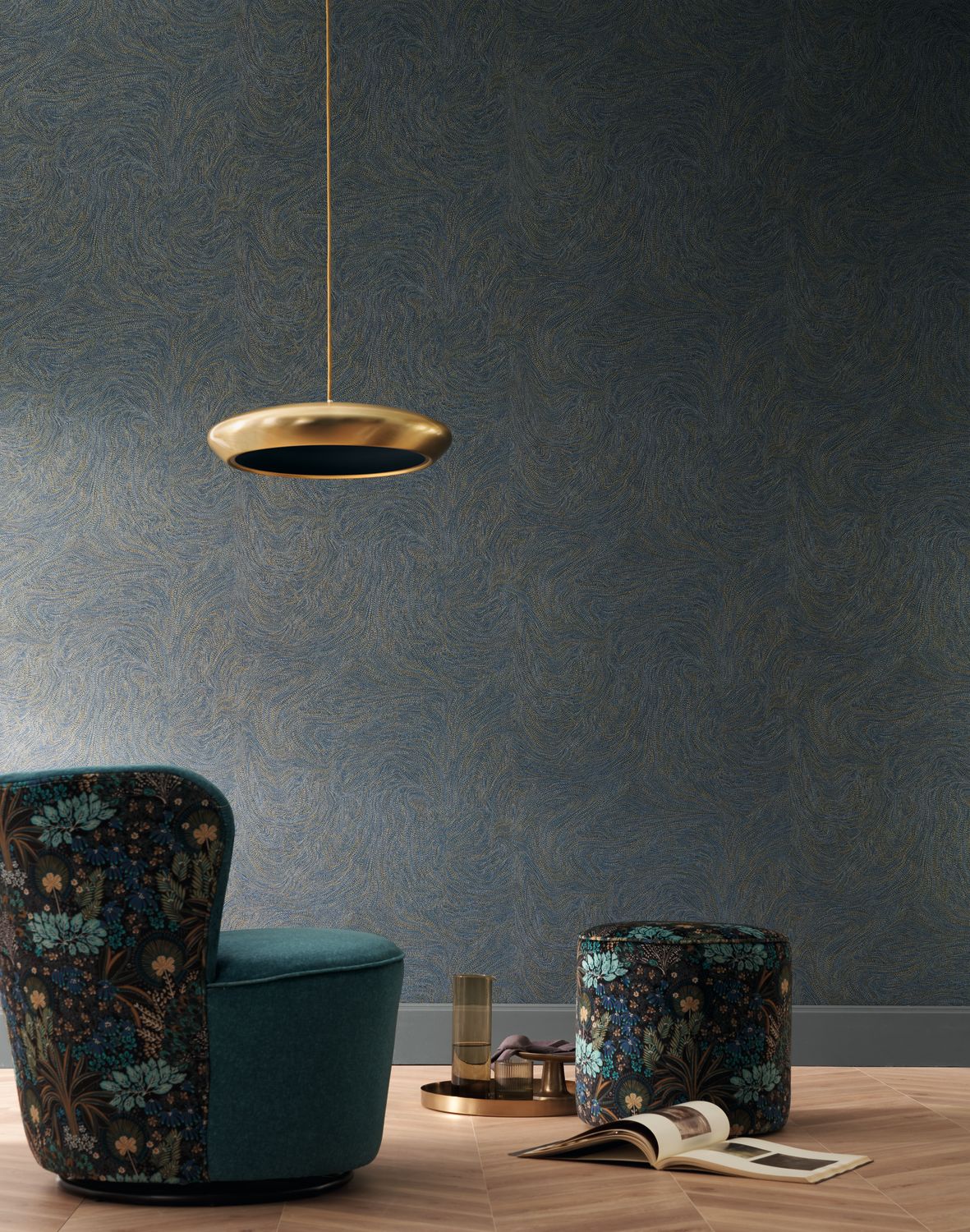 Voie lactee wallpaper by Casamance in navy and gold, a swirling marbled texture styled behind a teal velvet armchair with a brass disc pendant