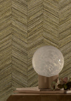 Ocotea wallpaper by Casamance in khaki, a chevron grasscloth weave styled behind a globe lamp on a timber plinth