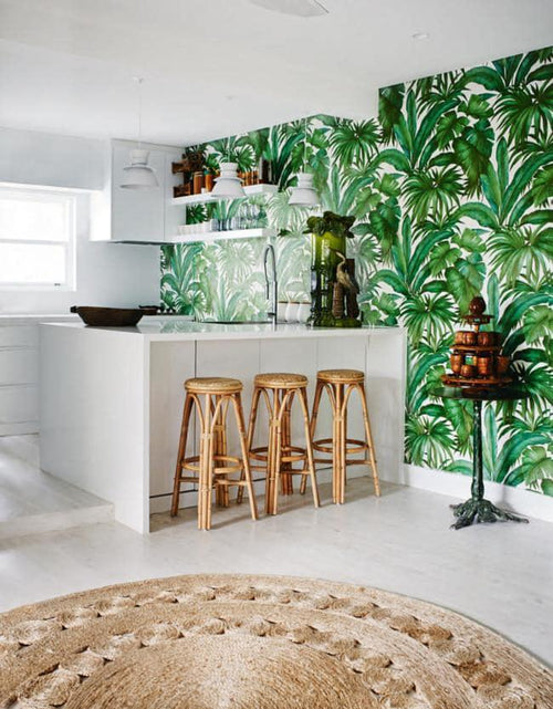 Green Giungla Palm wallpaper by Versace styled in a white coastal kitchen behind rattan bar stools