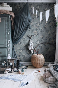 Sandra Floral wallpaper by Sandberg in slate blue, styled in a childs room with a canopy bed, bunting and a rattan apple