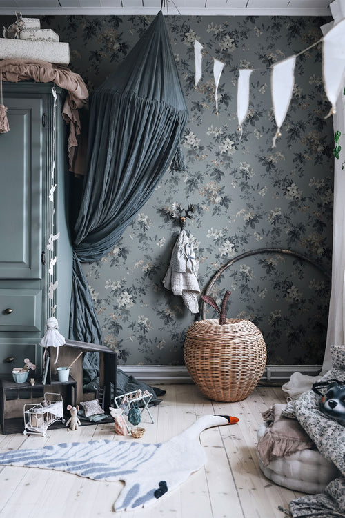 Sandra Floral wallpaper by Sandberg in slate blue, styled in a childs room with a canopy bed, bunting and a rattan apple