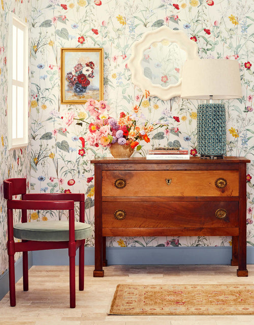 Ciao Bella White wallpaper by Wallpaper Trader styled in a room with a wooden chest, red chair and colourful wildflower